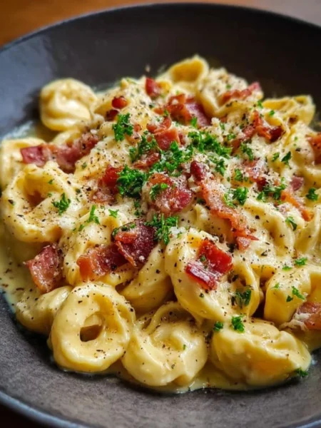 A bowl of creamy tortellini carbonara topped with bacon and parsley