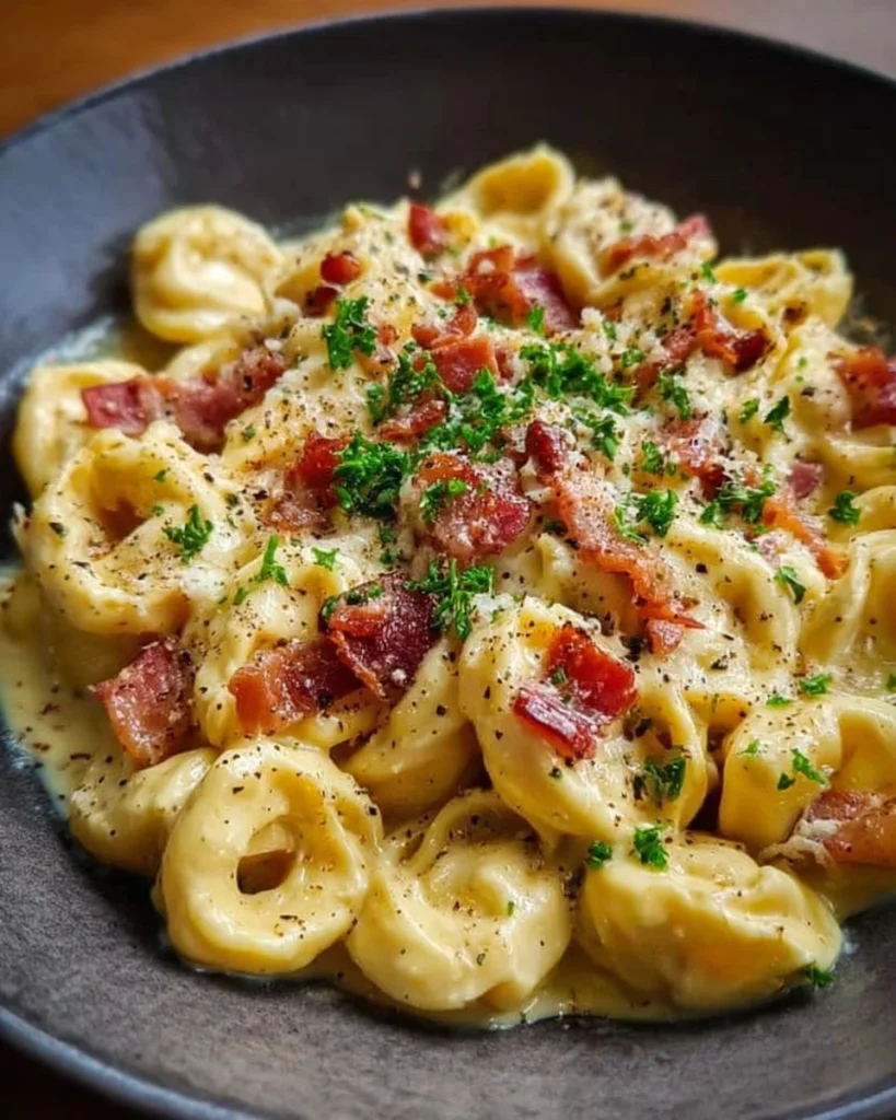 A bowl of creamy tortellini carbonara topped with bacon and parsley