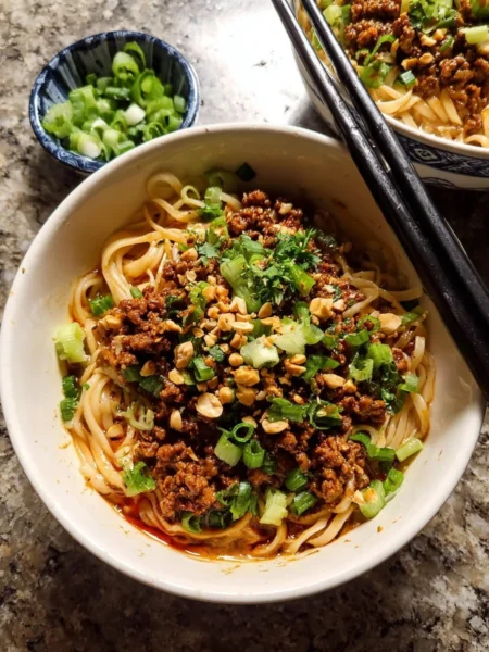 Bowl of Better Than Takeout Dan Dan Noodles garnished with scallions and peanuts