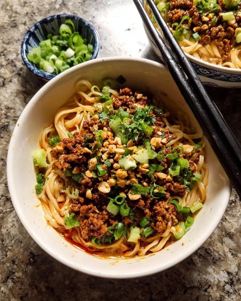 Bowl of Better Than Takeout Dan Dan Noodles garnished with scallions and peanuts