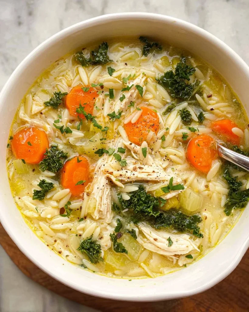 A bowl of lemon chicken orzo soup garnished with fresh herbs and lemon slices.