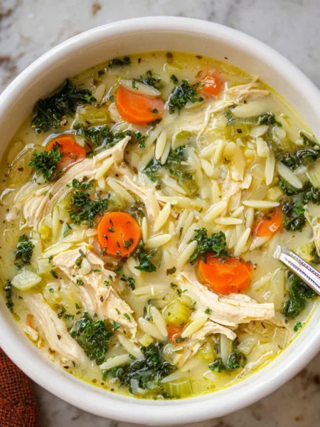 Bowl of Lemon Chicken Orzo Soup with fresh herbs and lemon slices